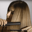 Cargar imagen en el visor de la galería, Chica castaña con mechas rubias con el pelo liso alisado pasándose una plancha de pelo con un peine