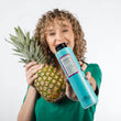 Cargar imagen en el visor de la galería, Chica rubia con pelo rizado sujetando champu COLOR BREEZE SHAMPOO y una piña natural