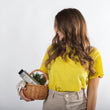 Cargar imagen en el visor de la galería, Chica castaña con pelo largo y ondulado mirando hacia un lado de su costado donde se encuentra una cesta de mimbre que contiene champu antigrasa YOUR BALANCE SHAMPOO y ramas de tomillo