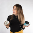 Cargar imagen en el visor de la galería, Chica rubia con mechas sonriendo con los ojos cerrados mientras sujeta medio coco y mascarilla nutritiva acondicionadora A MUST COCO MASK