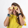 Cargar imagen en el visor de la galería, Chica con pelo castaño y largo sonriendo sacando la lengua sujetando un limón partido con cada mano delante de sus ojos