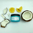 Cargar imagen en el visor de la galería, Mascarilla de coco y aceite de argan A MUST COCO MASK en el suelo rodeada de piezas de coco de todos los tamaños y limones partidos