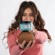 Cargar imagen en el visor de la galería, Chica con pelo castaño, largo y cuidado sujetando A MUST COCO MASK y un coco natural