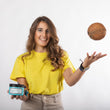 Cargar imagen en el visor de la galería, Chica con pelo castaño y ondulado sonriendo sujetando mascarilla natural A MUST COCO MASK y lanzando un coco al aire