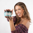 Cargar imagen en el visor de la galería, Chica sonriendo con pelo castaño con mechas rubias sujetando mascarilla reestructurante THE GLAM MASK con las dos mano delante de ella