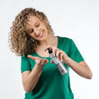 Cargar imagen en el visor de la galería, Chica rubia con pelo rizado sonriendo y echándose TROPICAL LEAVE IN en la mano con dispensador