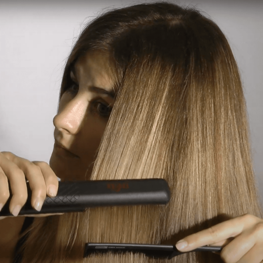 Chica castaña con mechas rubias con el pelo liso alisado pasándose una plancha de pelo con un peine