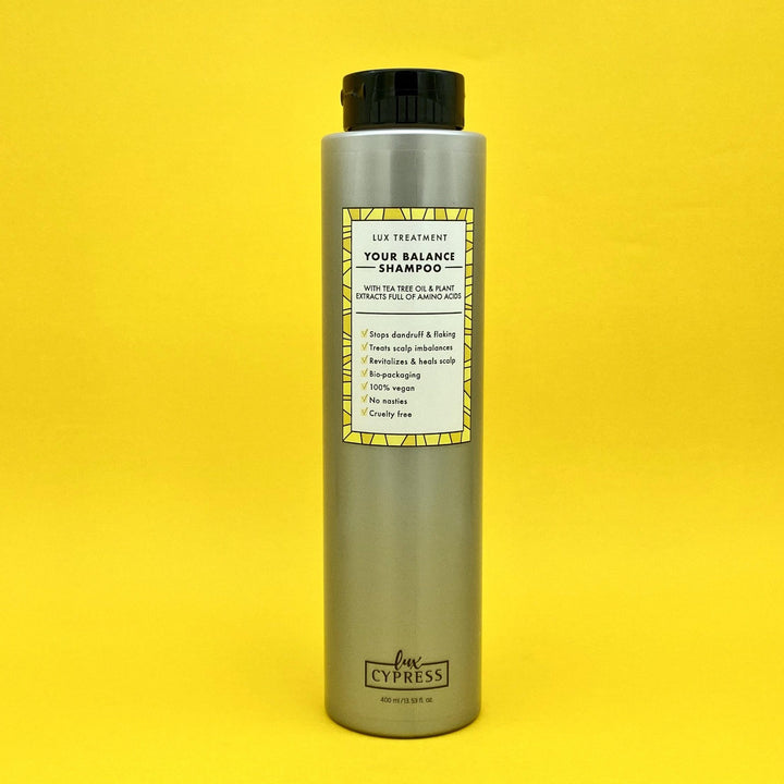 Champu tratamiento purificante para cuero cabelludo en bote alargado y color gris metalizado con etiqueta cuadrada con borde de tres tonalidades de amarillo e interior blanco con descripción y características de YOUR BALANCE SHAMPOO, logo de lux cypress en la parte inferior de champu, todo sobre fondo amarillo 