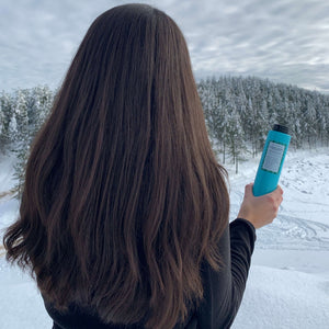 Chica morena con pelo largo, abundante y cuidado de espaldas mirando a la nieve sujetando champu natural sin sulfatos Marine Plasma Shampoo