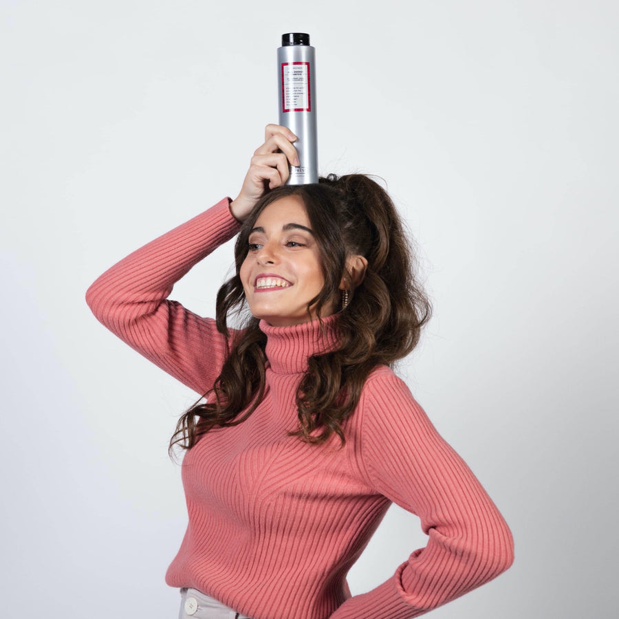 Chica sonriendo con pelo castaño y largo en una coleta con jersey rosa poniéndose champu anticaida FULL ENERGY SHAMPOO en la cabeza