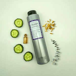 Champu violeta COOL BLONDE SHAMPOO tumbado en el suelo rodeado de calendula, eucalipto, un bote con miel y cuatro rodajas de pepino