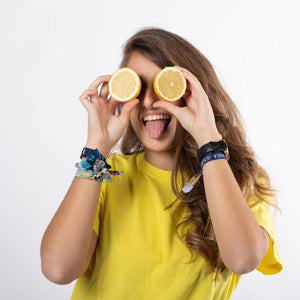 Chica  con pelo castaño y largo sonriendo sacando la lengua sujetando un limón partido con cada mano delante de sus ojos