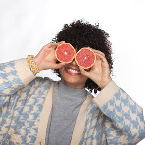 Chica con pelo rizado afro sonriendo y sujetando un pomelo abierto en cada mano delante de sus ojos