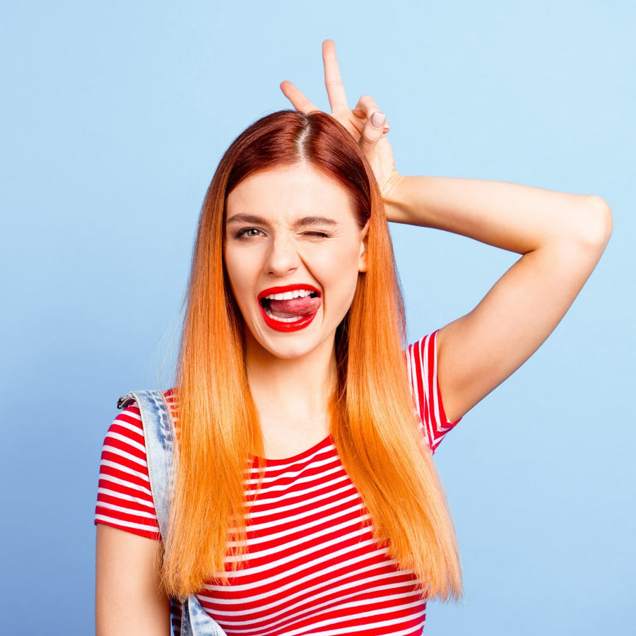 Chica con tinte naranja balayage con pelo liso alisado haciendo una mueca guiñando un ojo y sacando la lengua 