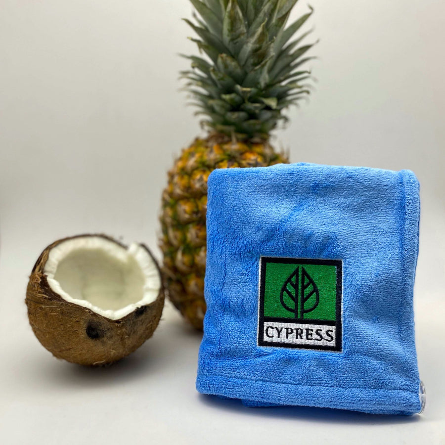 Turbante Cypress azul doblado en un cuadrado delante de una piña entera y medio coco